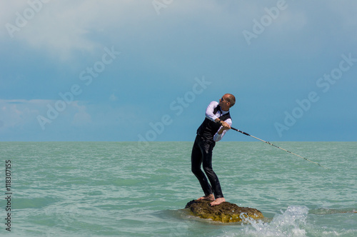 A man in a suit, with a fishing rod, fishing on a desert island