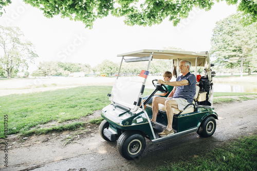 Grandfather and grandson in golf cart on golf course photo