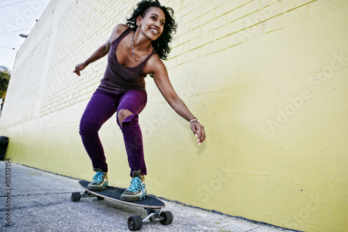 Hispanic woman riding skateboard on city street