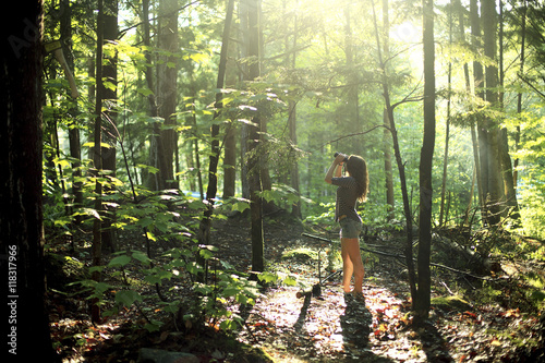 Girl looking through binoculars in forest photo