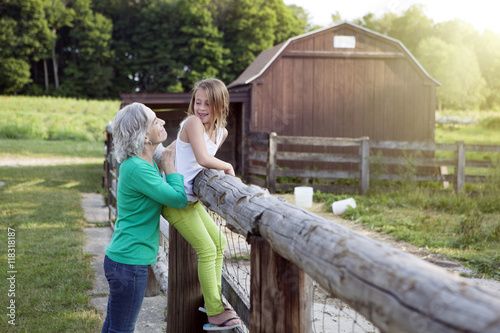 Caucasian grandmother and granddaughter smiling at farm fence