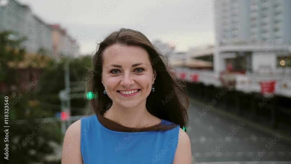 Wind blows long dark hair beautiful young women. happy, smiling girl standing on the bridge and looks at the camera Wind blows long dark hair beautiful young women. happy, smiling girl standing on the bridge and looks at the camera