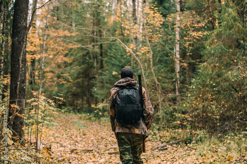 Male hunter in the autumn forest. A man holding a gun.