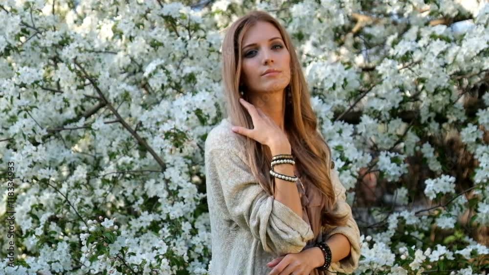 Beautiful young woman in long dress boho style under apple tree in blossom in Spring garden Beautiful young woman in long dress boho style under apple tree in blossom in Spring garden