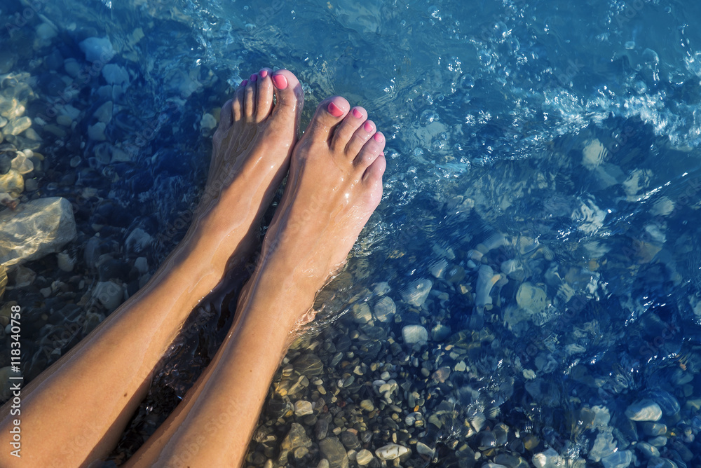 Young and beautiful female bare feet with red painted nails standing on a beach under waves.