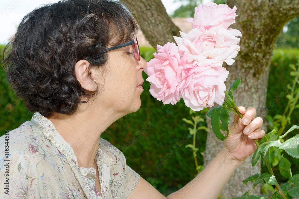 Obraz premium mature woman smelling the rose of her garden