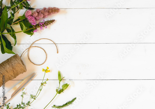 Wildflowers, thread and scissors on a white wooden background. T