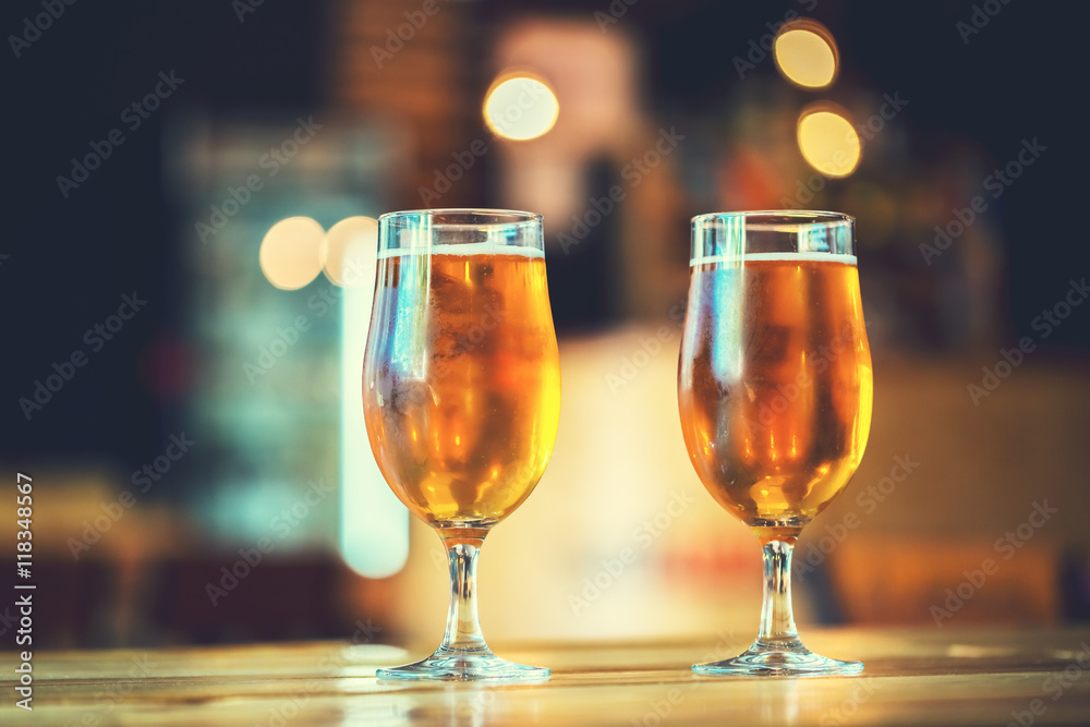 Two glasses of fresh cold light beer on a wooden bar counter in pub with free space for your text. Beautiful background of the Oktoberfest. Two glasses of fresh cold light beer on a wooden bar counter in pub with free space for your text. Beautiful background of the Oktoberfest.