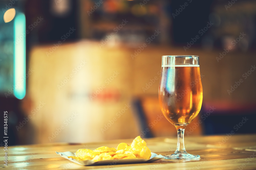 A fresh glass of cold light beer and potato chips on the wooden bar counter in pub with free space for your text. Beautiful background of the Oktoberfest.