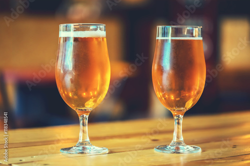 Two glasses of fresh cold light beer on a wooden bar counter in pub with free space for your text. Beautiful background of the Oktoberfest.