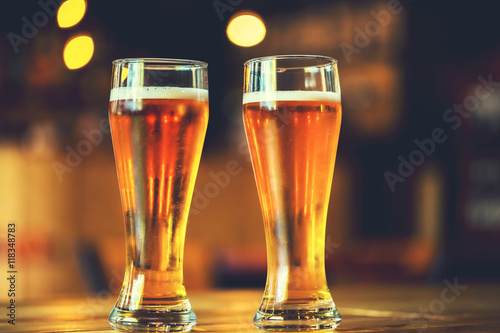 Fotografie Two glasses of fresh cold light beer on a wooden bar counter in pub with free space for your text