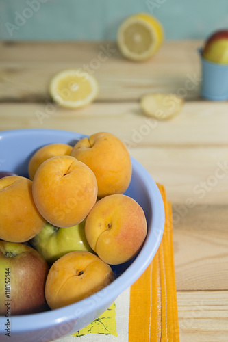 Apricots and apples in blue plastic bowl on wooden table.
