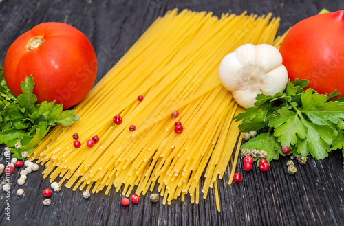 Raw spaghetti with tomatoes, cheese and spices on black wooden b