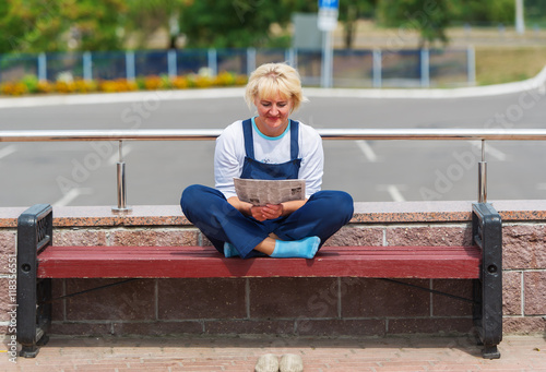 The woman in a uniform reads the newspaper on  city bench. © Irina84