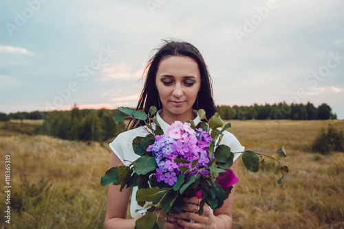 Outdoors portrait of a gorgeous young brunette woman holding lavender flowers.