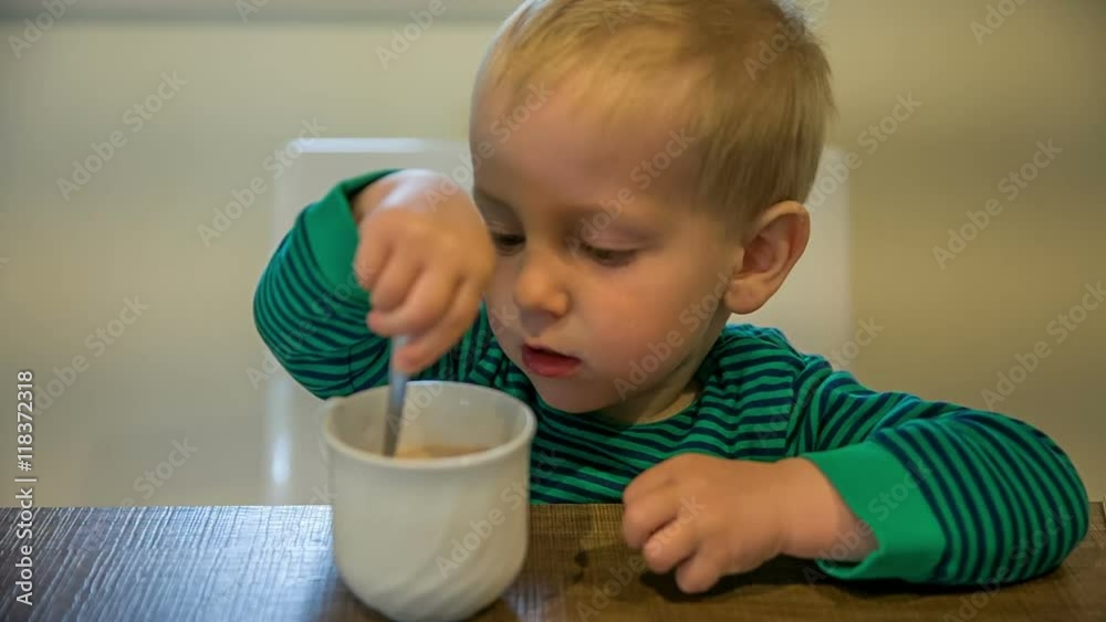 A toddler is sitting at a table in the kitchen and he is stirring the liquid in the cup. Then he pushes the cup away. His grandma comes. Close-up shot.
A toddler is sitting at a table in the kitchen and he is stirring the liquid in the cup. Then he pushes the cup away. His grandma comes. Close-up shot.