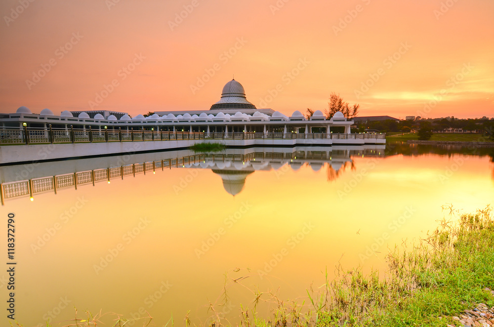 Beautiful white mosque during burning sunrise with mirror reflection on the lake