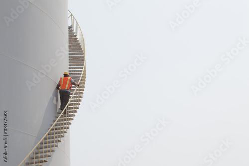 Mixed race worker climbing staircase on storage tank