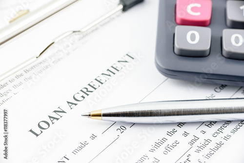 Blue ballpoint pen and a calculator on a loan agreement, preparation for filling and signing a form on a clipboard.