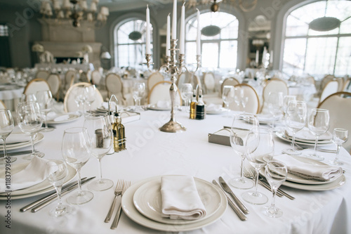Elegant wedding reception white table arrangement restaurant, 
candlestick on table. Plates, forks and glasses