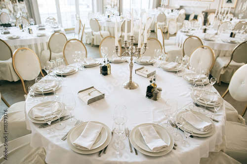 Elegant wedding reception white table arrangement restaurant, 
candlestick on table. Plates, forks and glasses