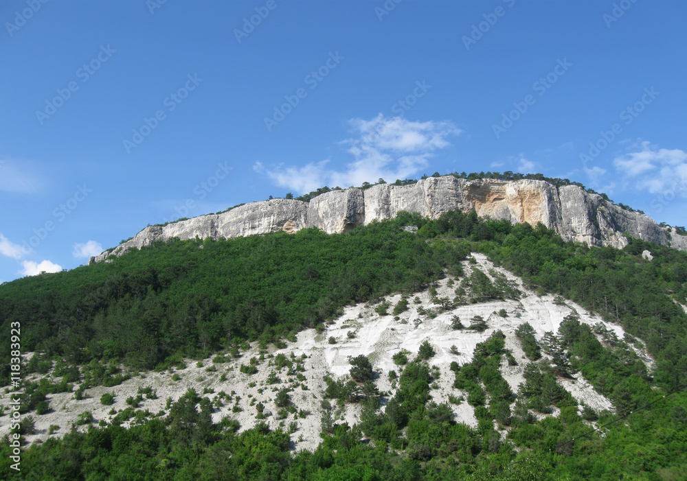 scenic white rock with green forested slopes on blue sky background, closeup, Crimea 