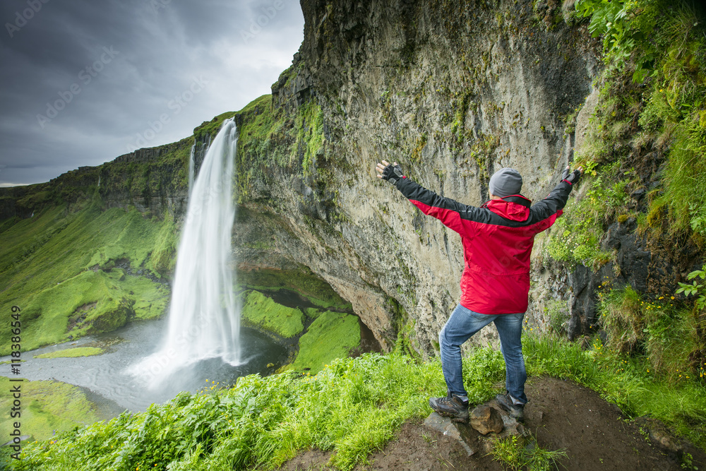 a man with lifted hands before waterfall in Iceland
