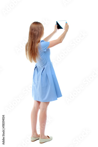 back view of standing young beautiful  woman  using a mobile phone. girl  watching. Rear view people collection.  backside view of person.  Isolated over white background. Skinny girl in blue dress © ghoststone