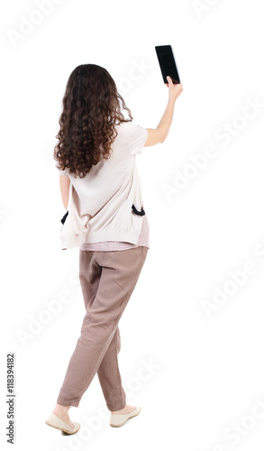 back view of standing young beautiful woman using a mobile phone. girl watching. Rear view people collection. backside view of person. Isolated over white background. Long-haired curly girl