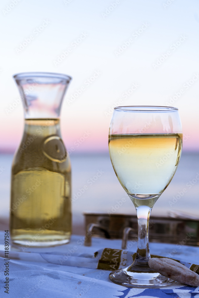 The carafe of white wine and a glass of wine on the beach, sunset, dinner by the sea, holiday, romance. Holidays in Greek wine in Greece.