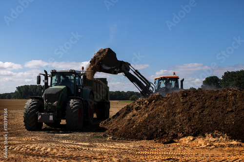 fertilize the field, excavator with shovel fills manure in the ttraile of a tractor