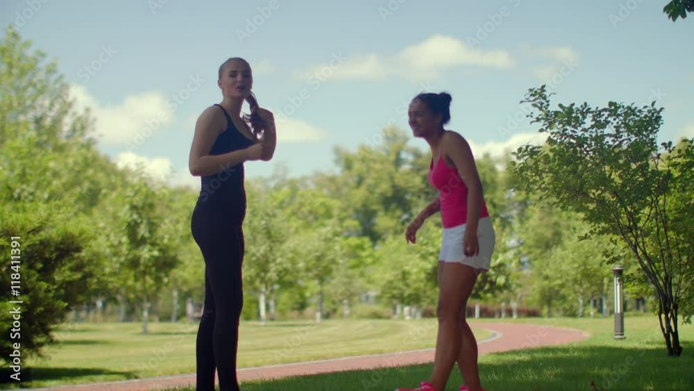 Fitness girls talking in park at summer day. Young female friends talking outdoor. Multiracial active lifestyle woman. Two fitness girls in sport clothes chatting together Fitness girls talking in park at summer day. Young female friends talking outdoor. Multiracial active lifestyle woman. Two fitness girls in sport clothes chatting together