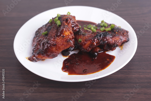 Grilled chicken or ayam golek on white plate, wooden background.