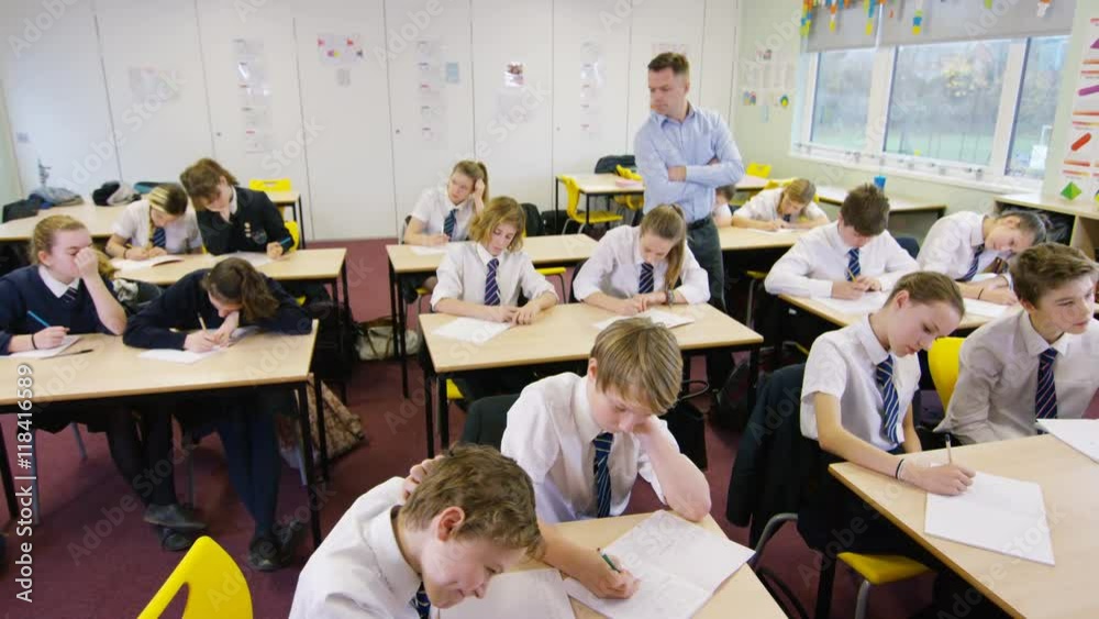  Teacher watching over young students working in school classroom