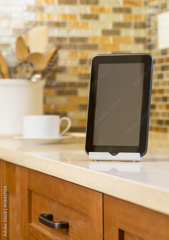 Close-up of tablet computer on stand on quartz countertop in contemporary upscale home kitchen. Selective focus on tablet. Close-up of tablet computer on stand on quartz countertop in contemporary upscale home kitchen. Selective focus on tablet.