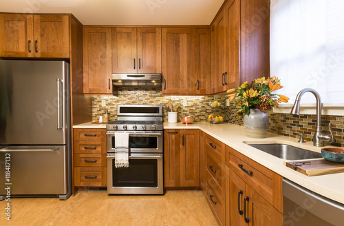 Contemporary upscale home kitchen interior with cherry wood cabinets, quartz countertops, sustainable recycled linoleum floors & stainless steel appliances including refrigerator & gas stove