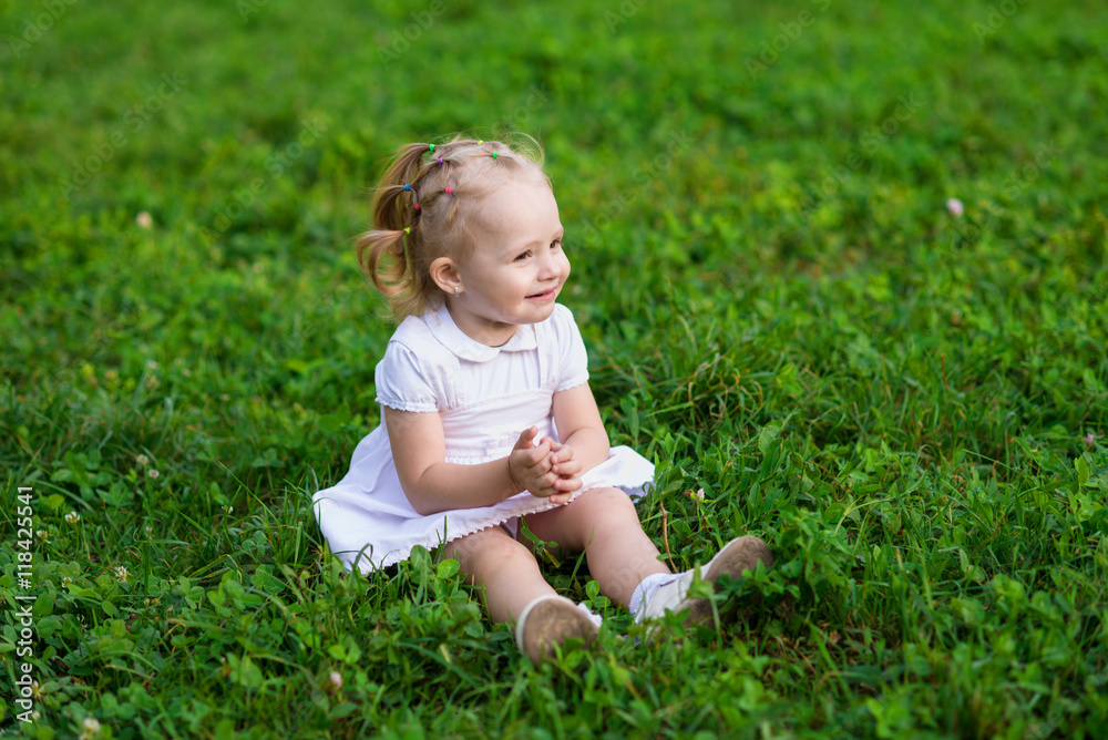 Baby girl in white dress sits and smiling on the fresh green grass Baby girl in white dress sits and smiling on the fresh green grass