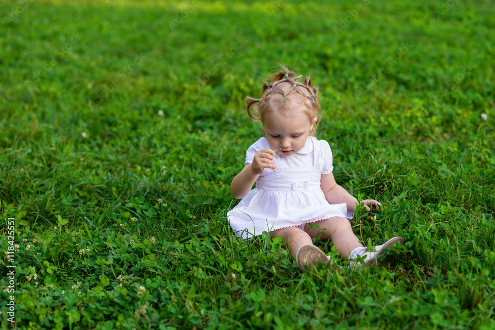Baby girl in white dress sits and smiling on the fresh green grass Baby girl in white dress sits and smiling on the fresh green grass