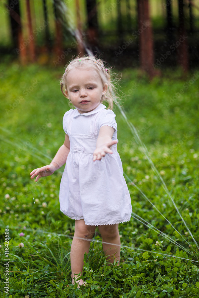 Little girl in white dress plays with sprinkler in the garden Little girl in white dress plays with sprinkler in the garden
