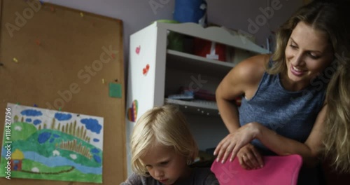 Smiling mom watching at her child drawing at table in nursery