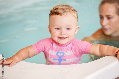Group portrait of white Caucasian mother and baby daughter playing in water diving in swimming pool inside, training to swim, healthy active lifestyle