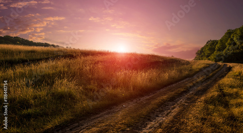 Field and a dirt road on the sunrise. magnificent picturesque scene. majestic sunset, amazing rural landscape