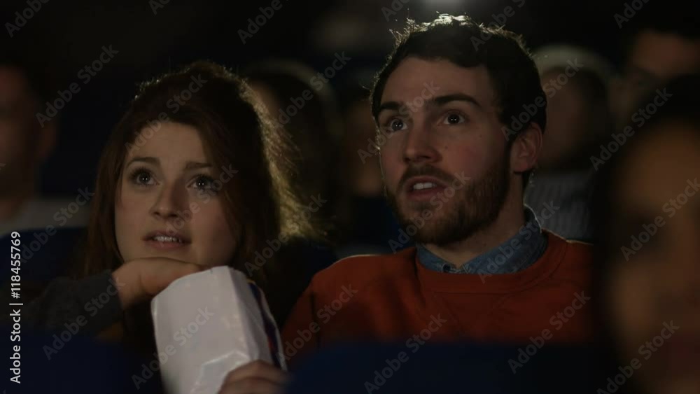 Cinema audience reacts to scary movie, with focus on young dating couple Cinema audience reacts to scary movie, with focus on young dating couple
