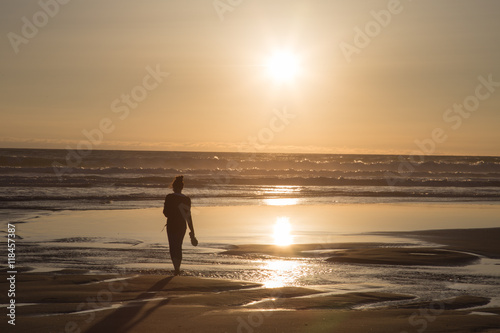 Silhouette of meditative, young woman watching sunset at the beach.