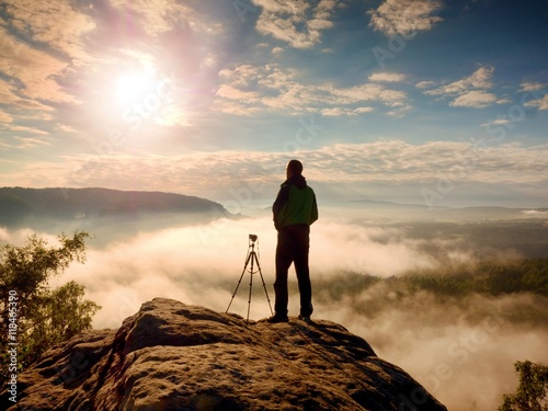 Professional photographer with tripod on cliff and thinking. Dreamy fog © rdonar
