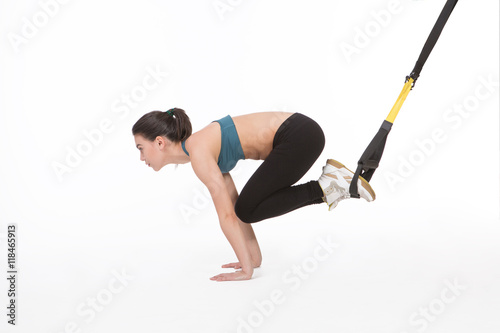Core body excercise concept. Image of young attractive woman doing suspension training with fitness straps in studio. Beautiful lady training with suspension trainer sling isolated on white. photo