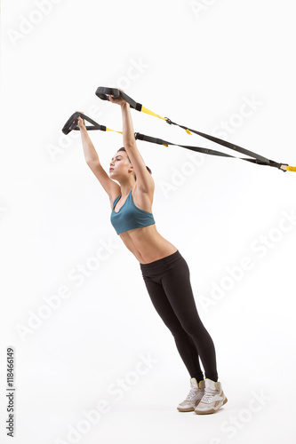 Upper body excercise concept on TRX. Beautiful young woman training with suspension trainer sling or suspension straps isolated on white background in studio.