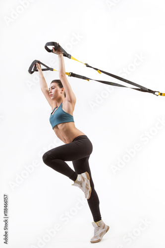 Low view of beautiful young woman training with suspension trainer sling or suspension straps isolated on white background in studio. Upper body excercise concept on TRX.