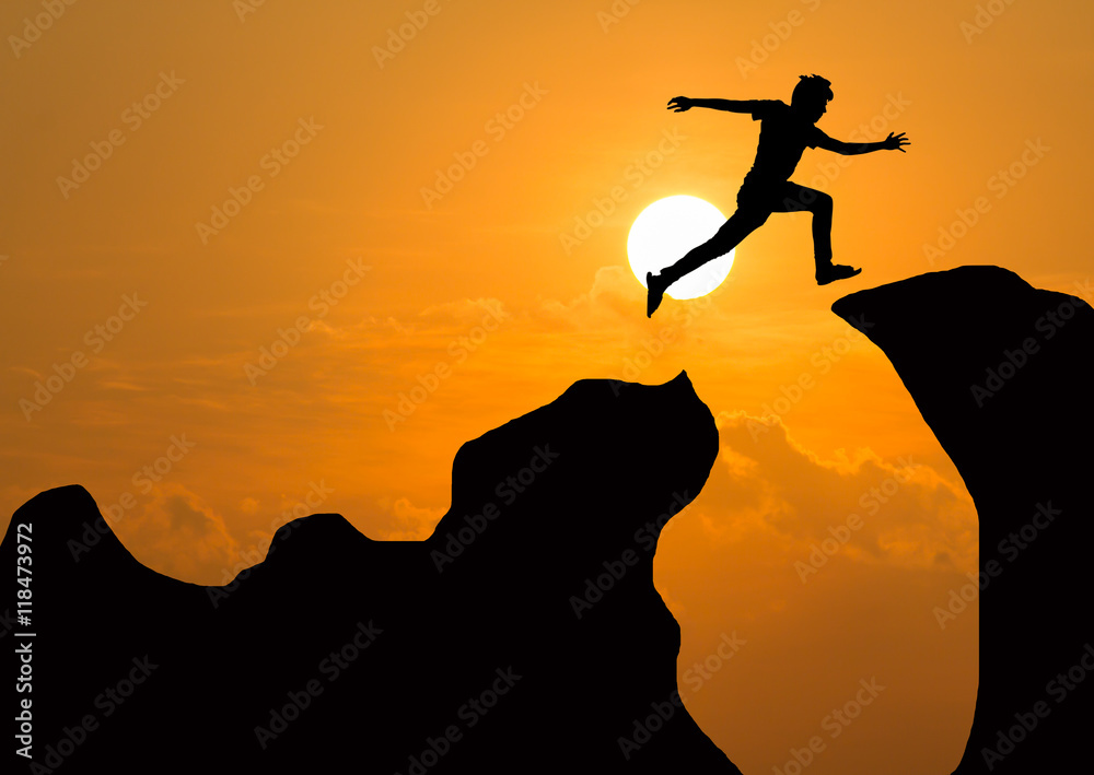 Silhouette of man jumping over cliff on sunset background