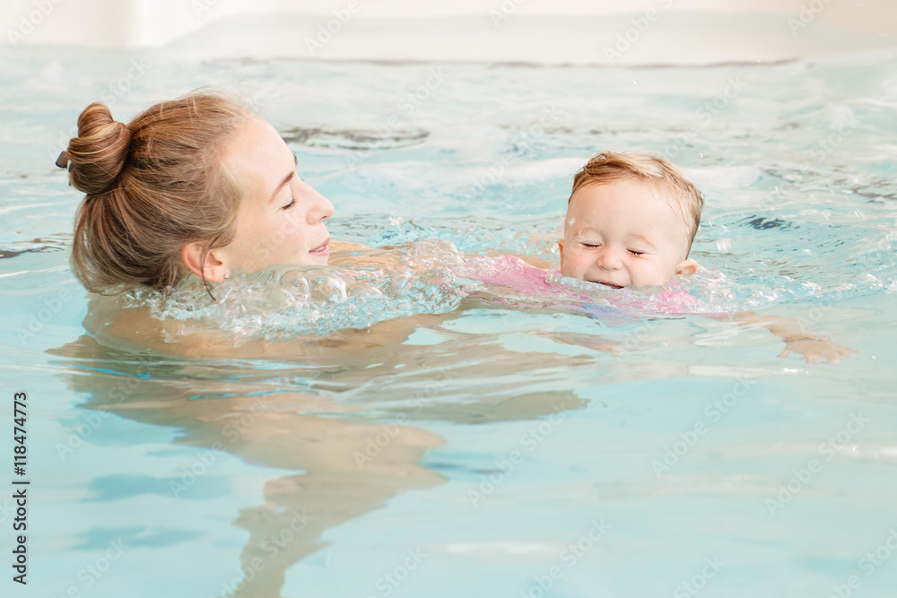 Group portrait of white Caucasian mother and baby daughter playing in water diving in swimming pool inside, training to swim, healthy active lifestyle Group portrait of white Caucasian mother and baby daughter playing in water diving in swimming pool inside, training to swim, healthy active lifestyle